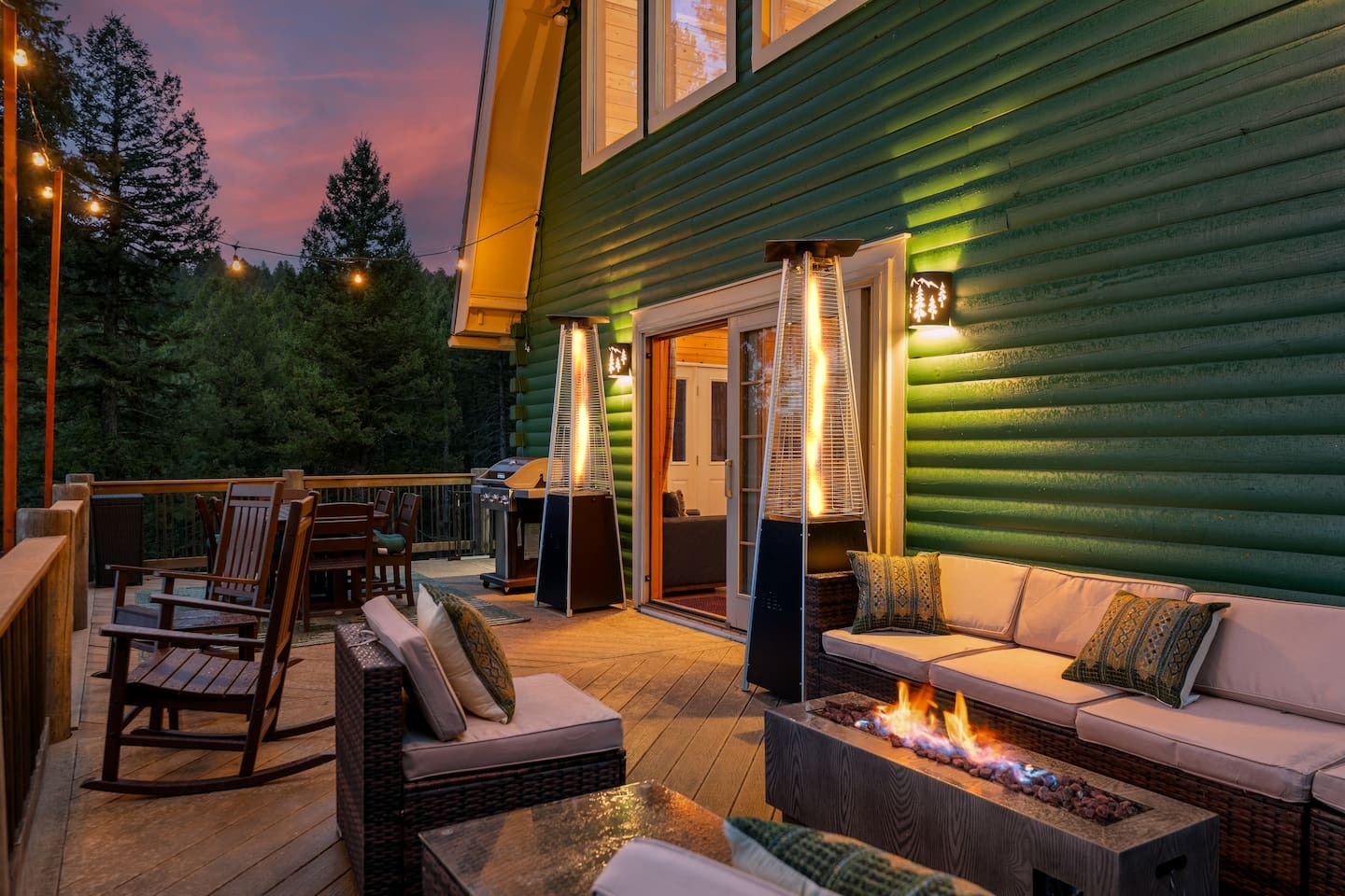 Deck lounge with a fire table at dusk beside the green siding