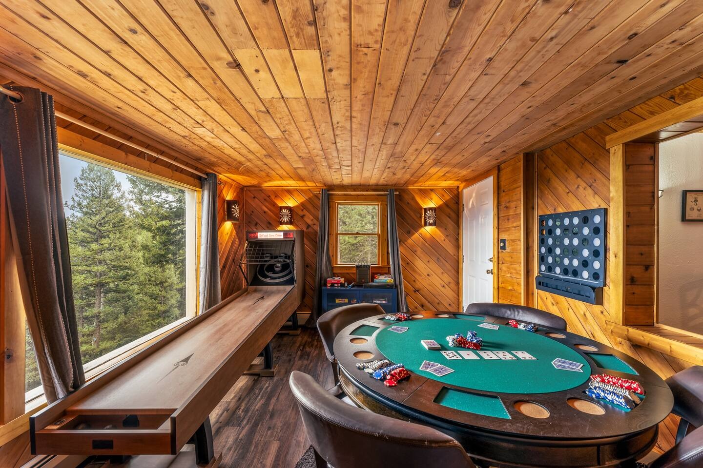 Game room with a poker table, a skee-ball machine and windows onto the pines