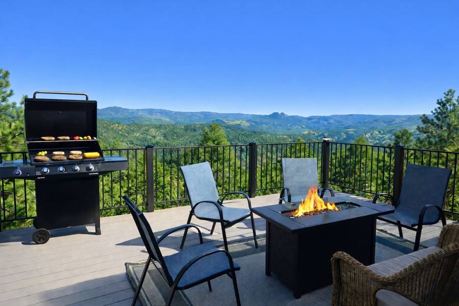 Deck with a fire table and grill above forested mountain ridges