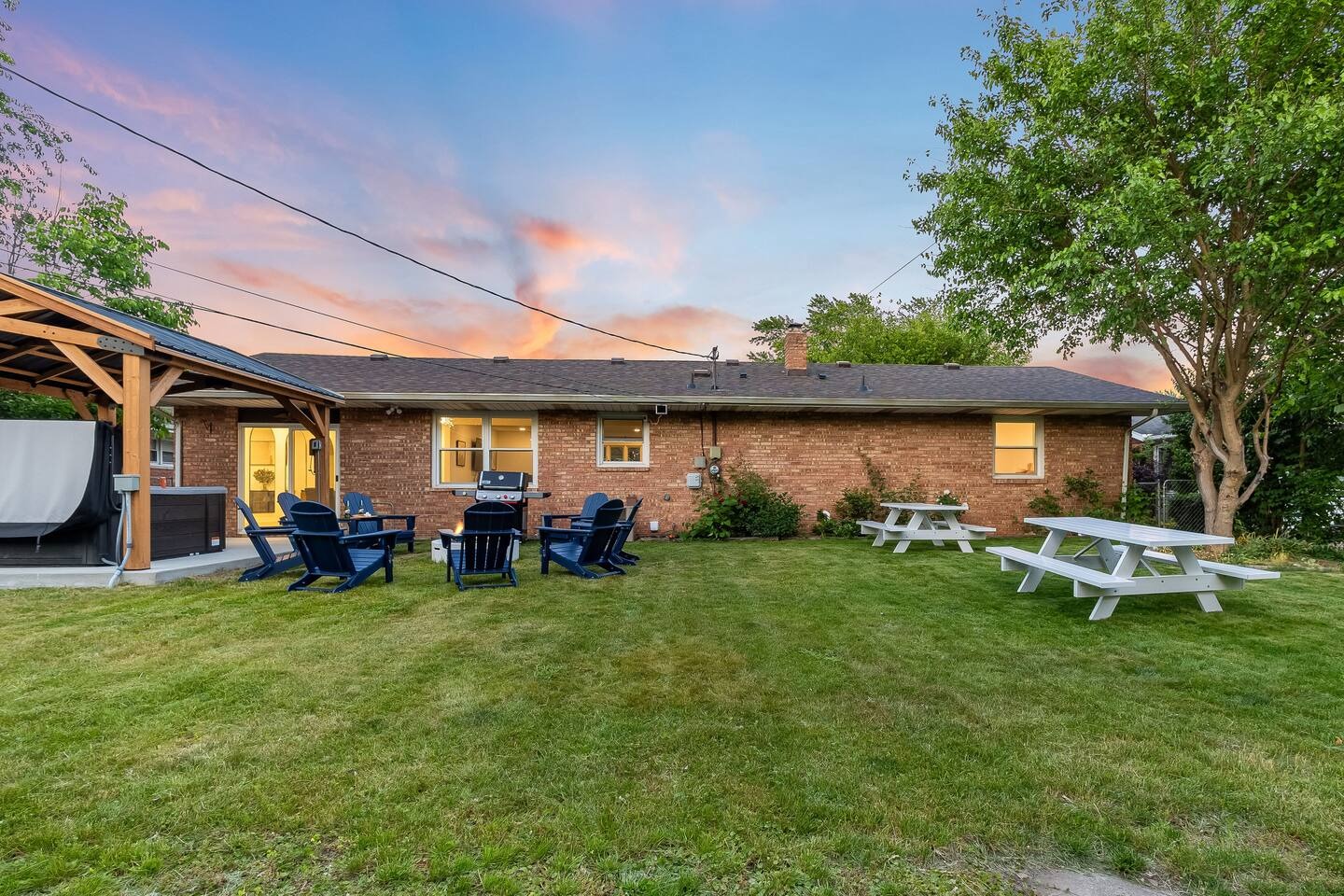 Wide backyard lawn with covered patio, fire pit and picnic tables at sunset