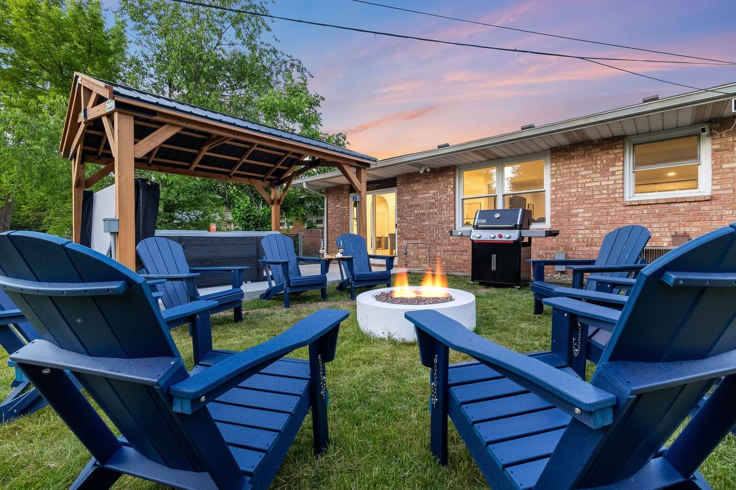 Adirondack chairs around the lit fire pit with the pergola behind
