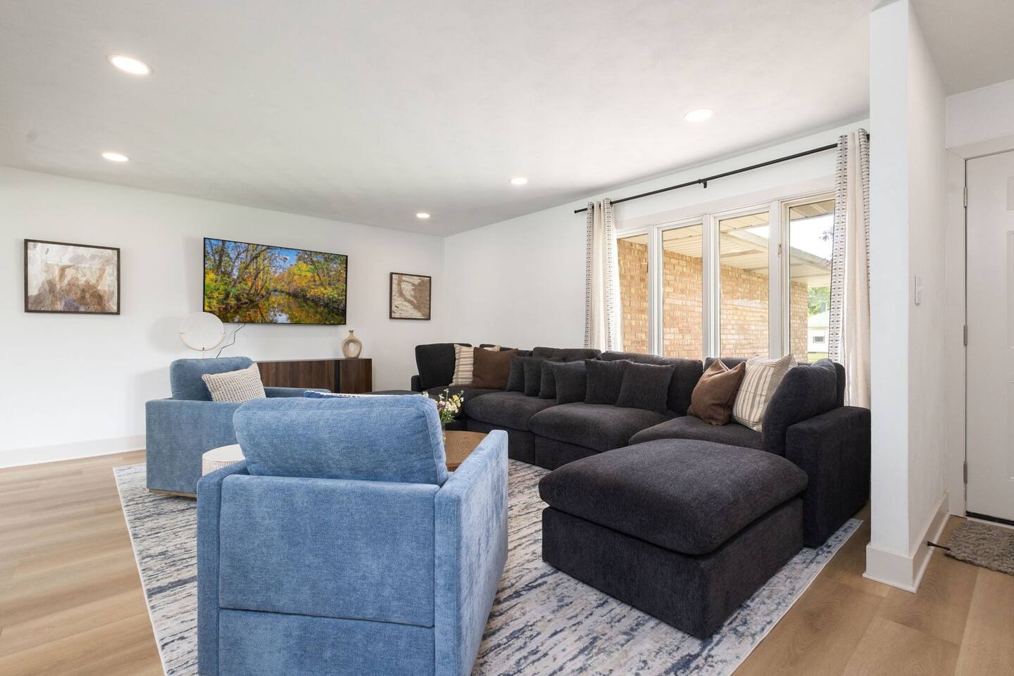 Bright main living room with a large navy sectional, blue armchairs and a mounted TV