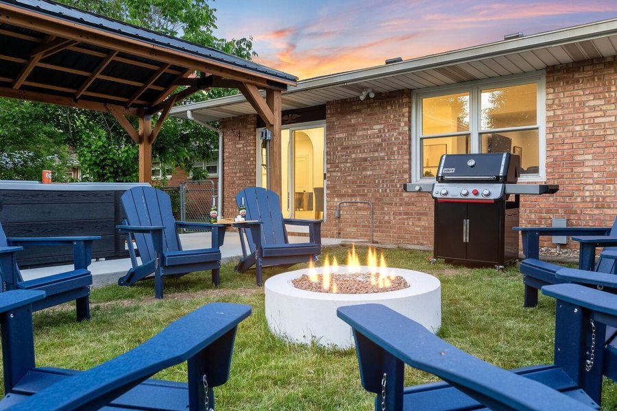Backyard at dusk with a covered patio, round fire pit and navy Adirondack chairs