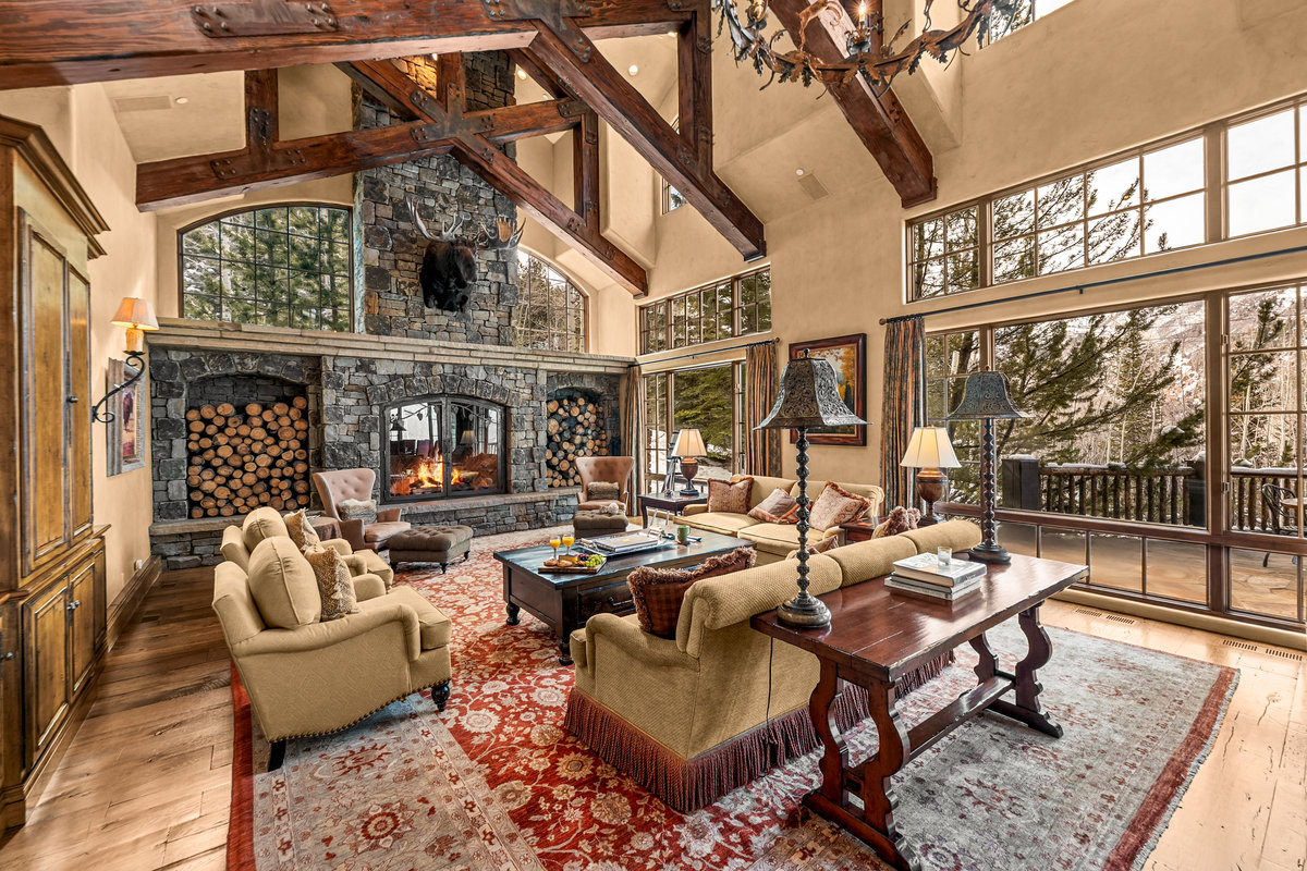 Great room with a stone hearth, timber beams and forest-view windows at The Lodge at Aspen Highlands