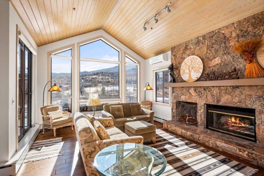 Vaulted living room with a stone fireplace and windows toward the ski area