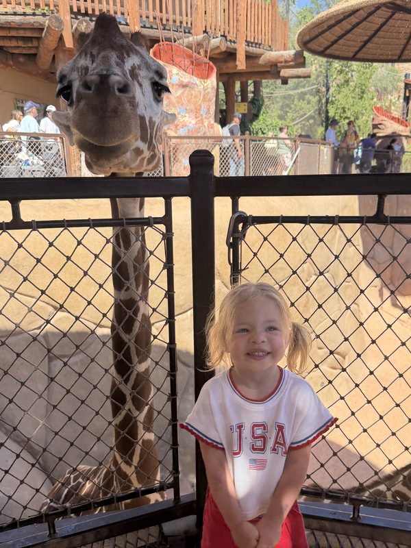 Daphne smiling at the zoo with a giraffe behind her